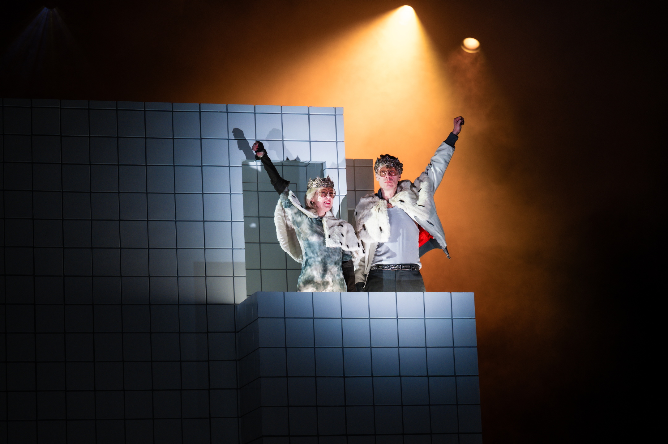 Mann og kvinne kledd i krone og kappe holder armene triumferende opp på balkong